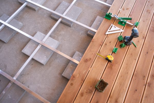Constructing a wooden deck involves measuring and placing tools carefully alongside materials on a flat surface.