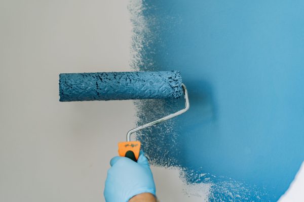 caucasian bearded man painting wall with paint roller. Painting apartment, renovating home with blue color paint. Image with selective focus