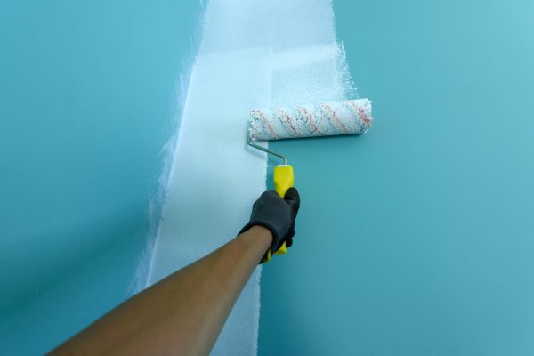 Hand with painting roller paint the wall in white color